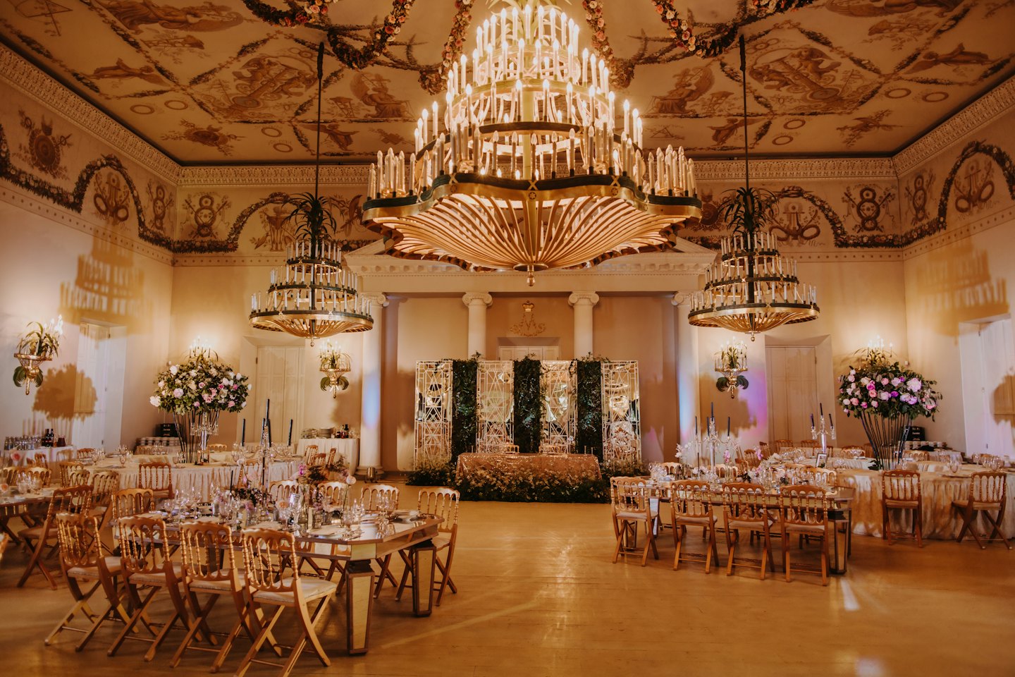 Elegancka sala balowa z formalnymi stołami i kwiatowymi dekoracjami na środku.